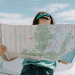 A woman looking at a map whilst sat on her car to show the the types of travel insurance that can protect her in the summer