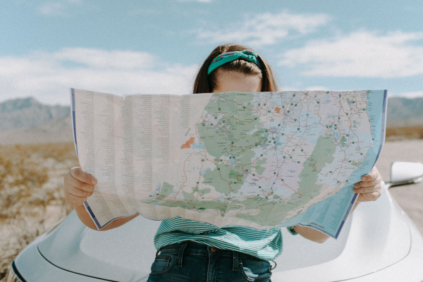 A woman looking at a map whilst sat on her car to show the the types of travel insurance that can protect her in the summer