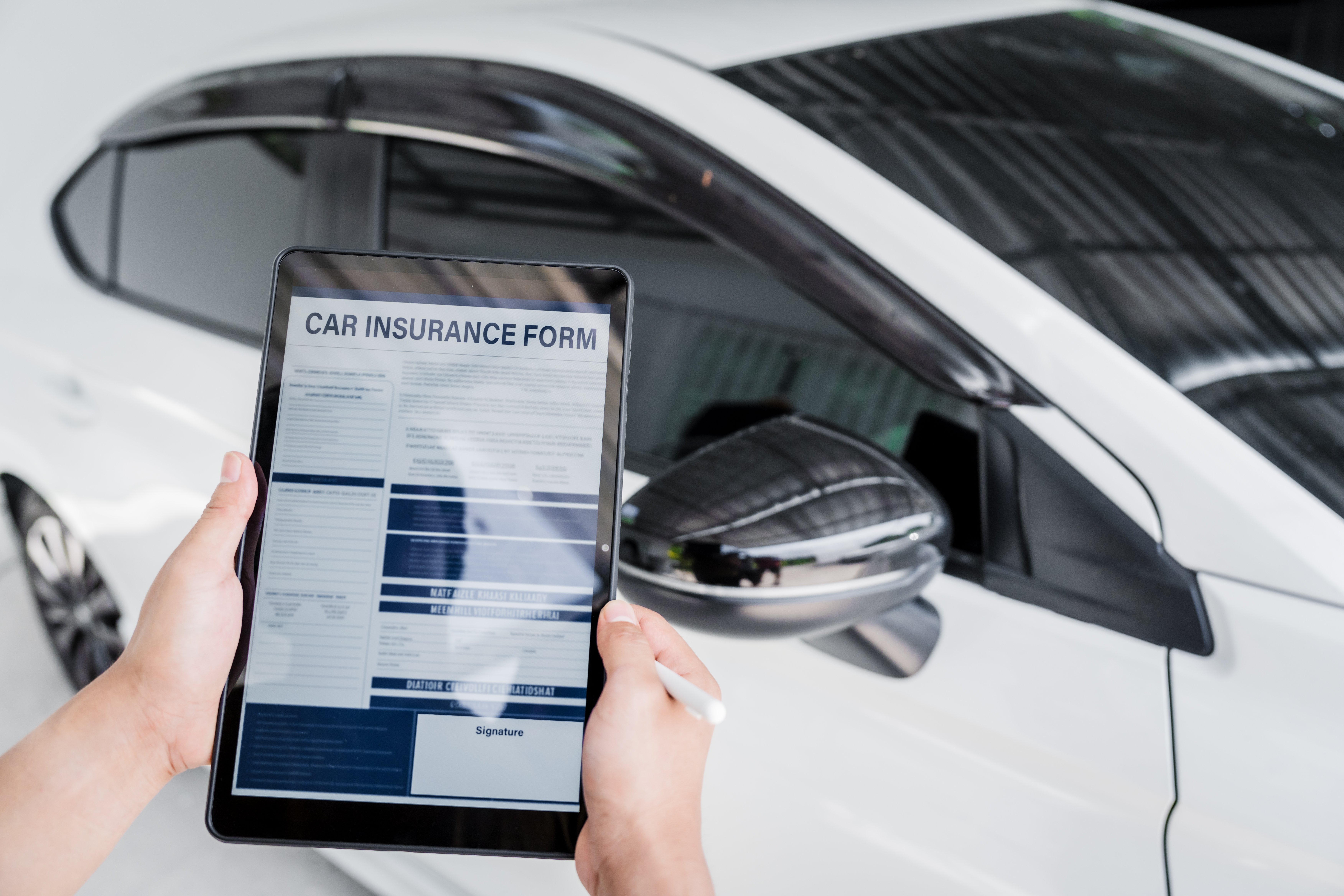 Person completing a digital insurance form beside a vehicle before MID Motor Trade database records are updated.